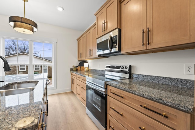 kitchen with pendant lighting, sink, dark stone countertops, stainless steel appliances, and light hardwood / wood-style floors