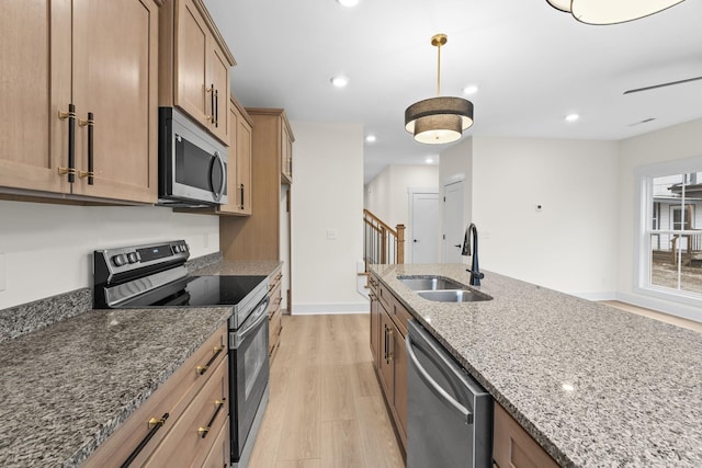 kitchen with sink, hanging light fixtures, stainless steel appliances, light stone countertops, and light hardwood / wood-style floors