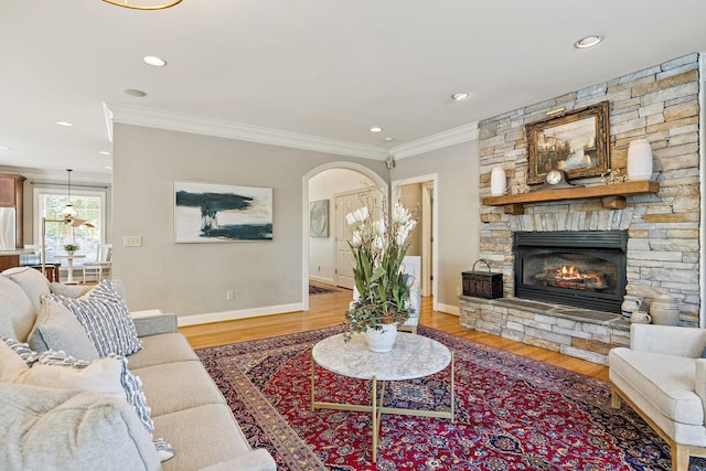 living room with crown molding, a stone fireplace, and light wood-type flooring