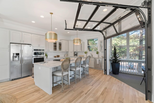 kitchen featuring appliances with stainless steel finishes, white cabinetry, hanging light fixtures, a center island, and light stone countertops