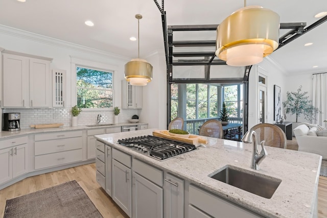 kitchen featuring stainless steel gas stovetop, crown molding, sink, and light stone counters