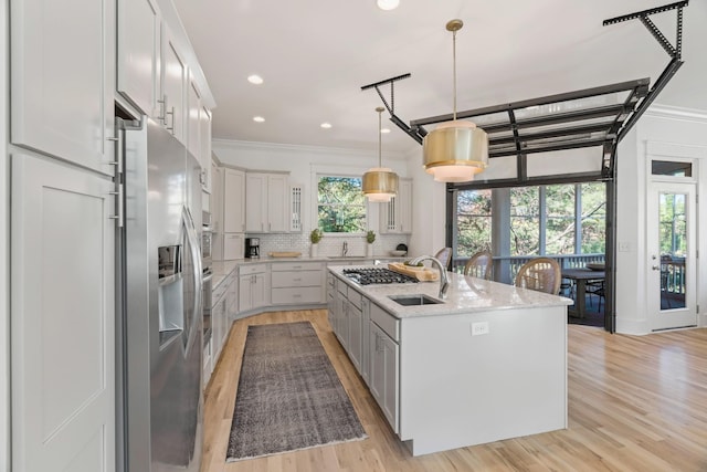 kitchen with sink, appliances with stainless steel finishes, pendant lighting, a kitchen island with sink, and backsplash