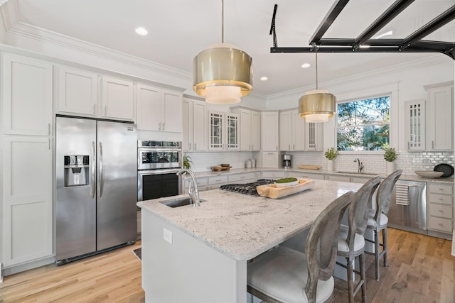 kitchen with a kitchen island with sink, decorative light fixtures, stainless steel appliances, and white cabinets