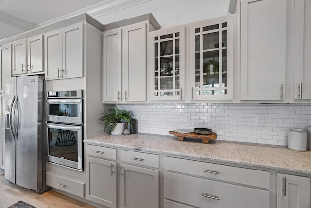 kitchen with light stone counters, crown molding, appliances with stainless steel finishes, light hardwood / wood-style floors, and decorative backsplash