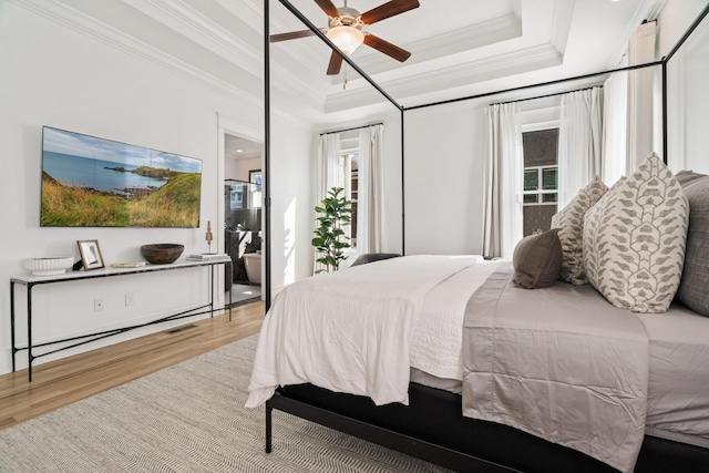 bedroom with multiple windows, a tray ceiling, light hardwood / wood-style flooring, and ornamental molding