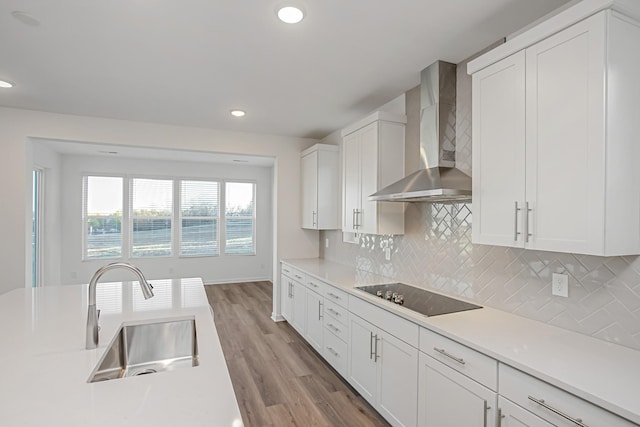 kitchen with black electric stovetop, wall chimney exhaust hood, sink, and white cabinets