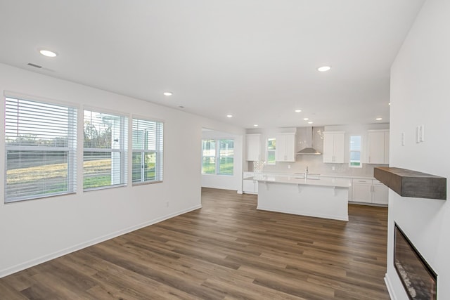 kitchen with wall chimney exhaust hood, a center island with sink, dark hardwood / wood-style floors, decorative backsplash, and white cabinets