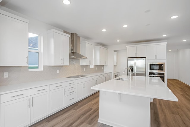 kitchen with sink, white cabinetry, appliances with stainless steel finishes, a kitchen island with sink, and wall chimney range hood