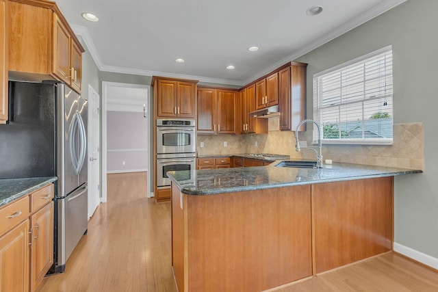 kitchen with appliances with stainless steel finishes, sink, dark stone counters, kitchen peninsula, and crown molding