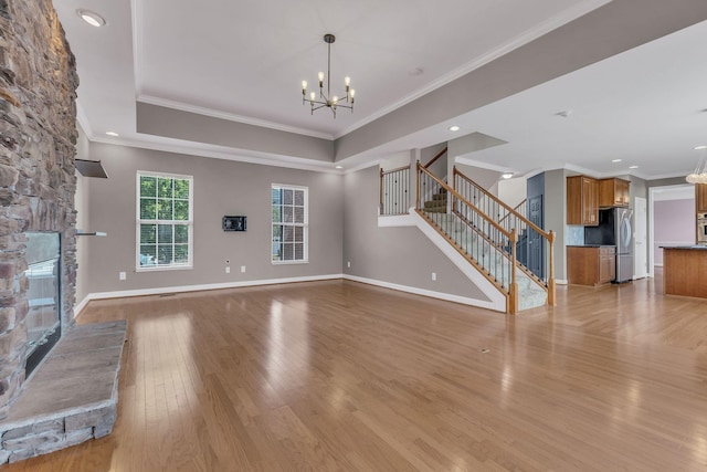 unfurnished living room featuring light hardwood / wood-style flooring, an inviting chandelier, a tray ceiling, ornamental molding, and a stone fireplace