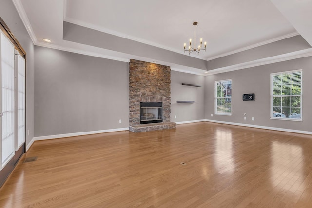 unfurnished living room with crown molding, a notable chandelier, a tray ceiling, light hardwood / wood-style floors, and a stone fireplace