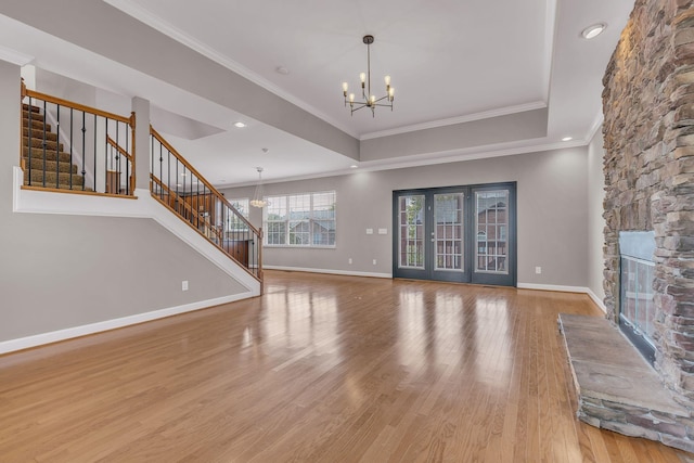 unfurnished living room featuring ornamental molding, a stone fireplace, light wood-type flooring, and an inviting chandelier