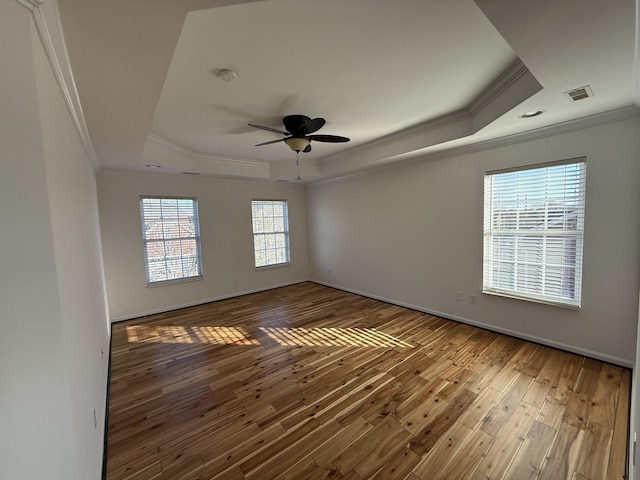 empty room with crown molding, hardwood / wood-style floors, a tray ceiling, and ceiling fan