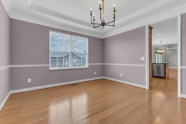 unfurnished room with ornamental molding, a tray ceiling, an inviting chandelier, and light hardwood / wood-style flooring