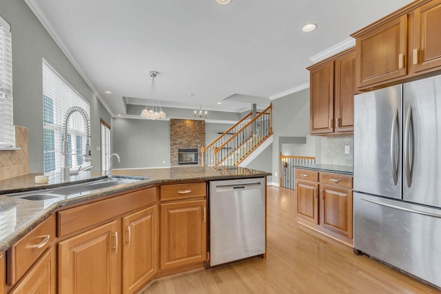 kitchen with appliances with stainless steel finishes, sink, dark stone countertops, ornamental molding, and light wood-type flooring