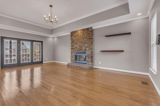 unfurnished living room featuring crown molding, hardwood / wood-style floors, a notable chandelier, a tray ceiling, and a fireplace