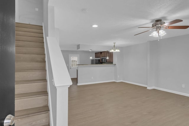 stairway with hardwood / wood-style flooring, ceiling fan with notable chandelier, and a textured ceiling