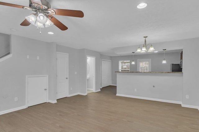 unfurnished living room with ceiling fan with notable chandelier and light hardwood / wood-style floors