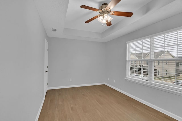 empty room featuring a tray ceiling, light hardwood / wood-style floors, and ceiling fan