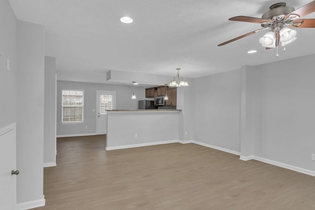 unfurnished living room featuring wood-type flooring, ceiling fan with notable chandelier, and a textured ceiling