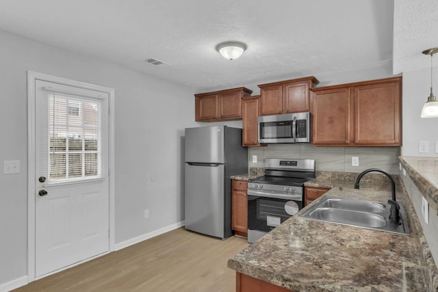 kitchen featuring sink, tasteful backsplash, hanging light fixtures, appliances with stainless steel finishes, and light hardwood / wood-style floors