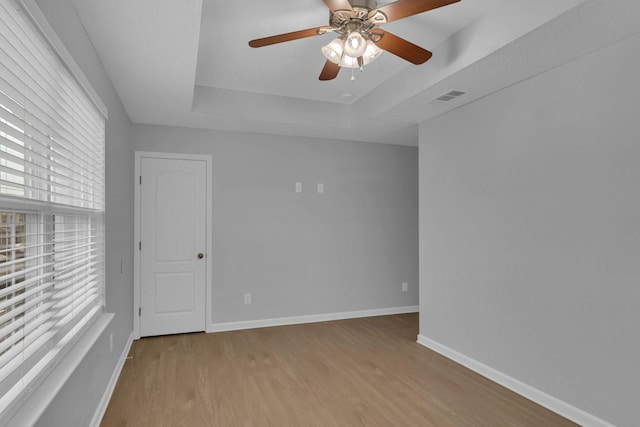 unfurnished room with ceiling fan, a raised ceiling, and light wood-type flooring