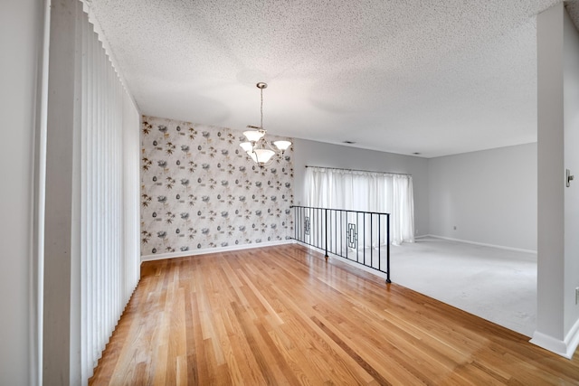 empty room with wood-type flooring, a notable chandelier, and a textured ceiling