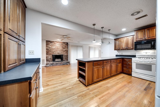 kitchen with hanging light fixtures, white gas range oven, kitchen peninsula, a brick fireplace, and light hardwood / wood-style flooring