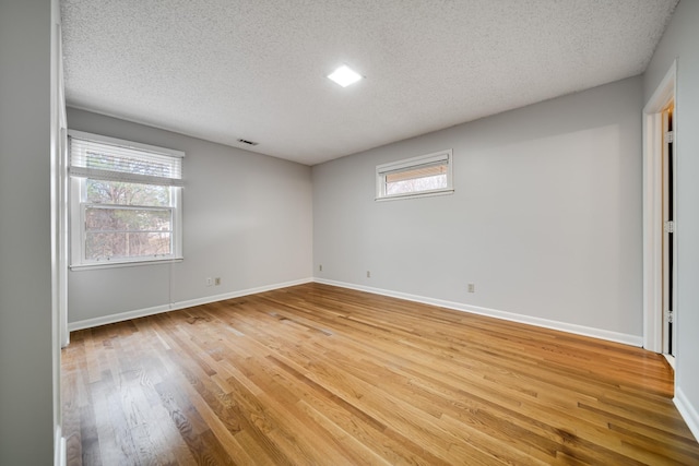 unfurnished room featuring plenty of natural light, a textured ceiling, and light wood-type flooring