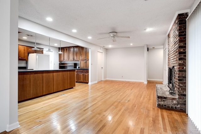 kitchen with decorative light fixtures, light hardwood / wood-style flooring, white refrigerator, ceiling fan, and a fireplace