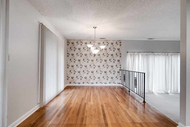 unfurnished dining area featuring an inviting chandelier, light hardwood / wood-style flooring, and a textured ceiling