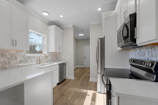 kitchen with appliances with stainless steel finishes, sink, white cabinets, crown molding, and light hardwood / wood-style flooring