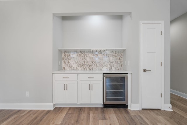 bar with beverage cooler, light wood-type flooring, decorative backsplash, and white cabinets