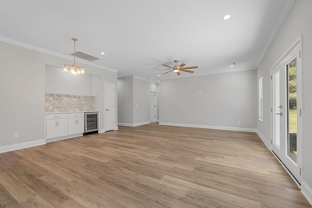 unfurnished living room with wine cooler, crown molding, ceiling fan with notable chandelier, and light wood-type flooring