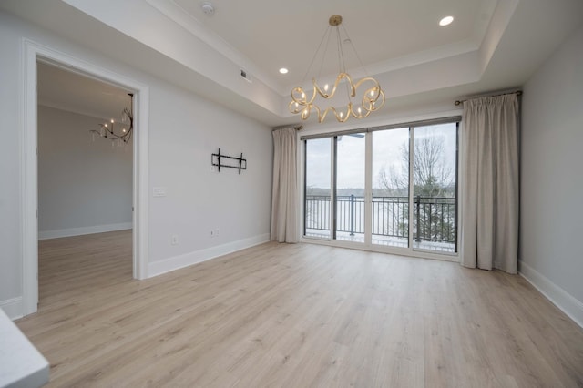 empty room with a raised ceiling, a chandelier, and light wood-type flooring