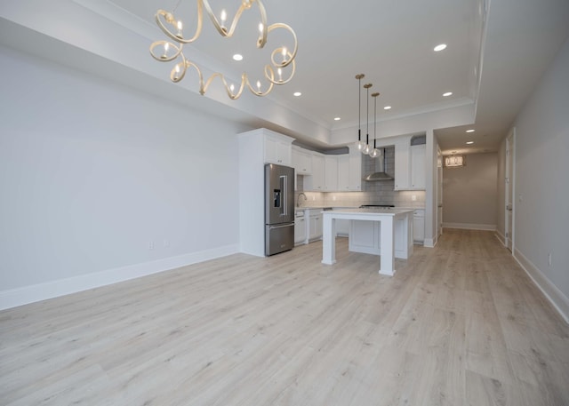 kitchen with wall chimney exhaust hood, high end fridge, decorative light fixtures, a kitchen island, and white cabinets