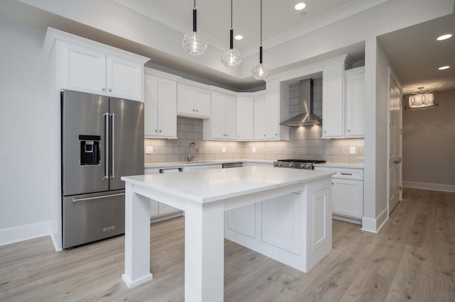 kitchen featuring wall chimney range hood, white cabinetry, high end refrigerator, and decorative light fixtures