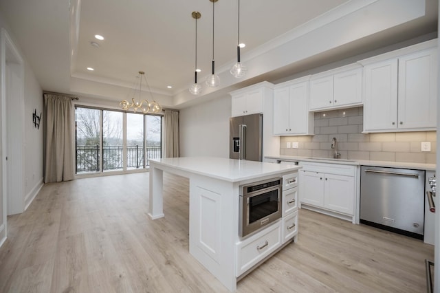 kitchen with pendant lighting, a raised ceiling, white cabinetry, sink, and stainless steel appliances