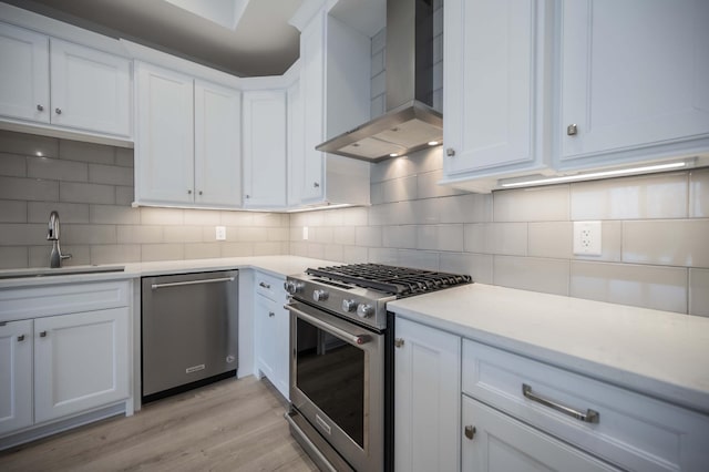 kitchen with wall chimney range hood, stainless steel appliances, sink, and white cabinets