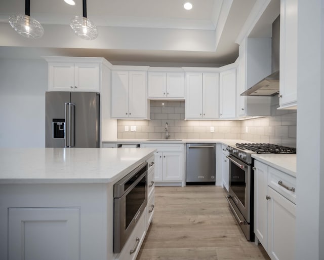 kitchen featuring wall chimney range hood, sink, appliances with stainless steel finishes, white cabinetry, and hanging light fixtures