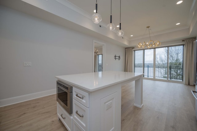 kitchen with a kitchen island, decorative light fixtures, white cabinets, light hardwood / wood-style floors, and a raised ceiling