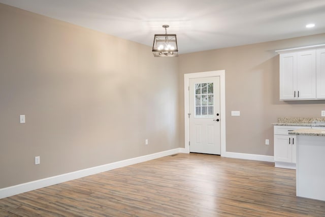 unfurnished dining area featuring a notable chandelier, baseboards, and wood finished floors