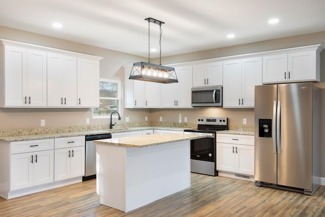 kitchen featuring white cabinets, a center island, stainless steel appliances, light wood-style floors, and pendant lighting