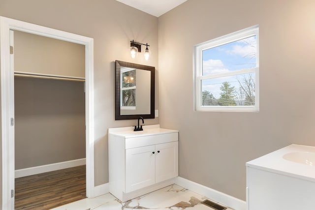 full bath with baseboards, visible vents, two vanities, a walk in closet, and a sink