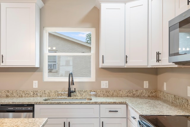 kitchen featuring appliances with stainless steel finishes, a sink, white cabinetry, and light stone countertops