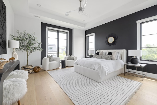 bedroom with multiple windows, a tray ceiling, and light wood-type flooring