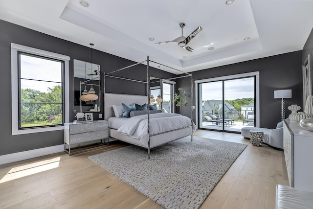 bedroom with access to exterior, a tray ceiling, and light hardwood / wood-style floors