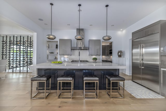 kitchen featuring wall chimney exhaust hood, appliances with stainless steel finishes, decorative light fixtures, and an island with sink