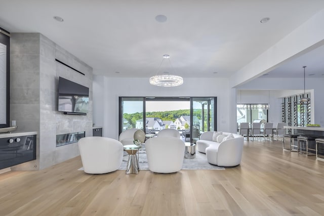 living room featuring a tiled fireplace, an inviting chandelier, and light wood-type flooring