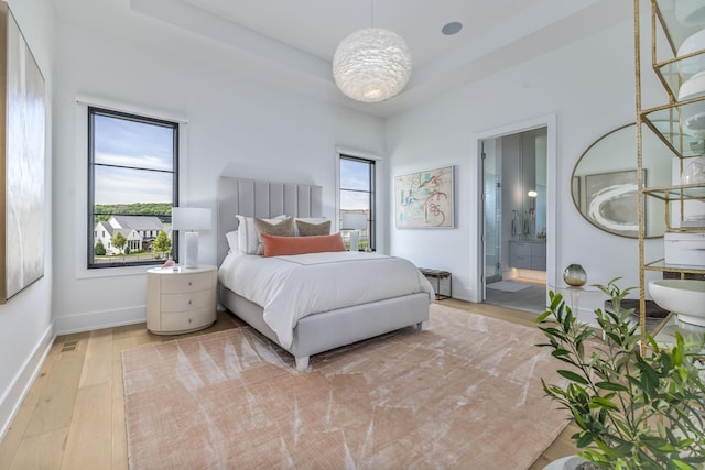 bedroom with multiple windows, ensuite bath, light hardwood / wood-style floors, and a raised ceiling